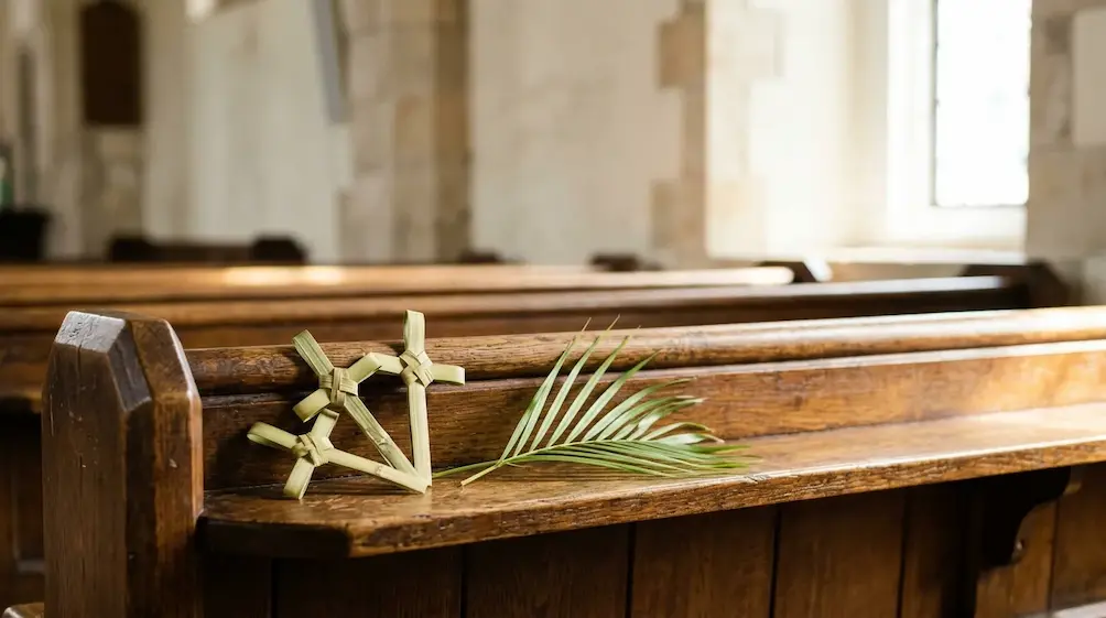 Small woven palm crosses resting on a wooden church pew in soft window light